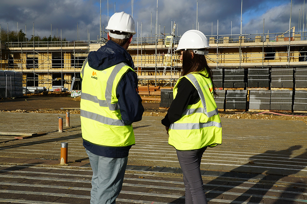 Two surveyors looking at b uildings in construction, wearing hard hats and high visibility jackets